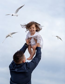 Father lifting his daughter into the sky with seagulls around
